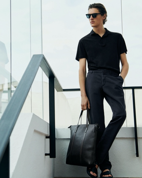 A young man with slicked back hair wearing a short-sleeve Massimo Dutti shirt, dress pants and a matching leather bag