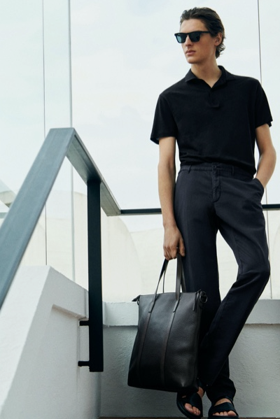 A young man with slicked back hair wearing a short-sleeve Massimo Dutti shirt, dress pants and a matching leather bag