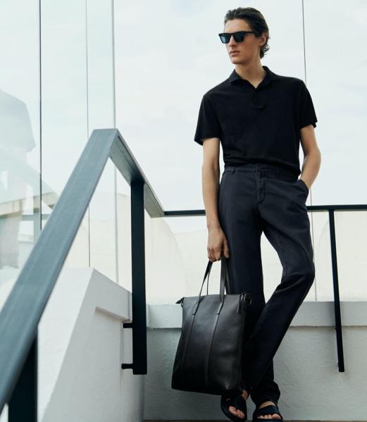 A young man with slicked back hair wearing a short-sleeve Massimo Dutti shirt, dress pants and a matching leather bag