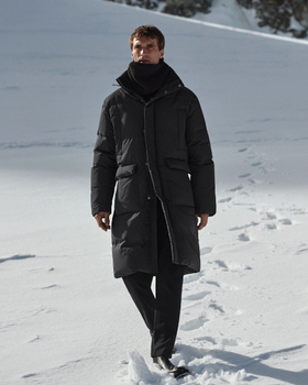 A man bundled up wearing a dark grey COS jacket, scarf and pants walking in the snow