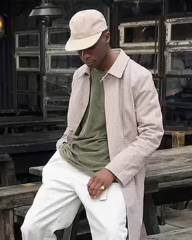 A man wearing an Asos biege jacket, green t-shirt, white pants and a matching white hat