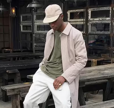 A man wearing an Asos biege jacket, green t-shirt, white pants and a matching white hat