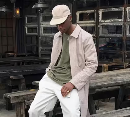 A man wearing an Asos biege jacket, green t-shirt, white pants and a matching white hat