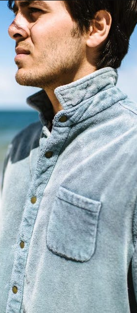 A man standing on the beach wearing an blue Adam Mar long-sleeve button up shirt