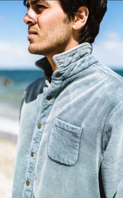 A man standing on the beach wearing an blue Adam Mar long-sleeve button up shirt
