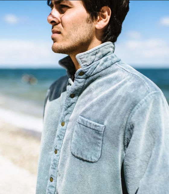 A man standing on the beach wearing an blue Adam Mar long-sleeve button up shirt