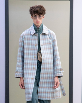 A man wearing a baby blue checkered print Maison Kitsune trench coat and clear vintage glasses