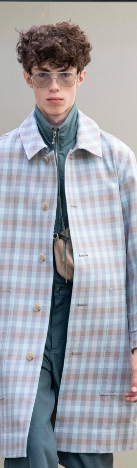 A man wearing a baby blue checkered print Maison Kitsune trench coat and clear vintage glasses