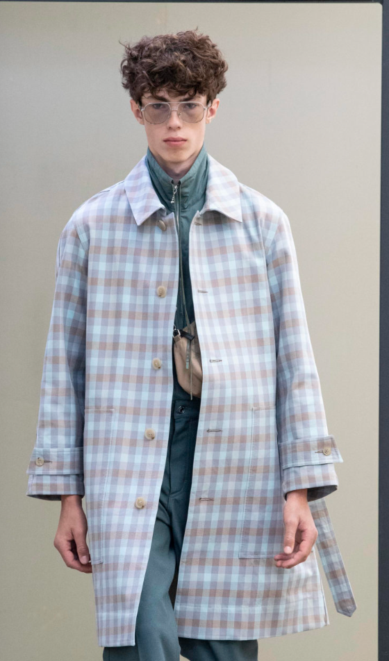 A man wearing a baby blue checkered print Maison Kitsune trench coat and clear vintage glasses