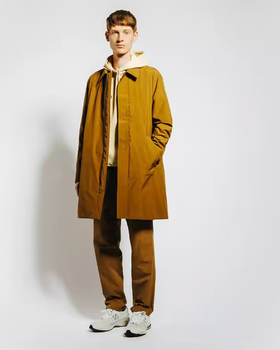 A man wearing a long light brown trench coat with matching pants and Oatmeal Sweatshirt along with New Balance Dad Shoes