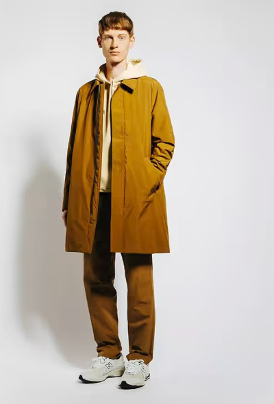 A man wearing a long light brown trench coat with matching pants and Oatmeal Sweatshirt along with New Balance Dad Shoes