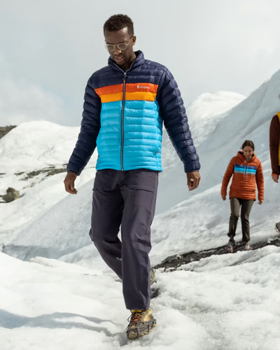 A group of people hiking on a snowy mountain wearing colorful CotoPaxi Puffy Jackets and active wear
