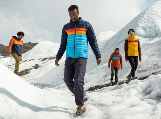 A group of people hiking on a snowy mountain wearing colorful CotoPaxi Puffy Jackets and active wear