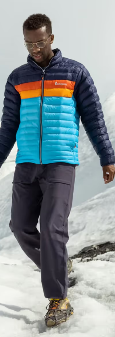 A group of people hiking on a snowy mountain wearing colorful CotoPaxi Puffy Jackets and active wear