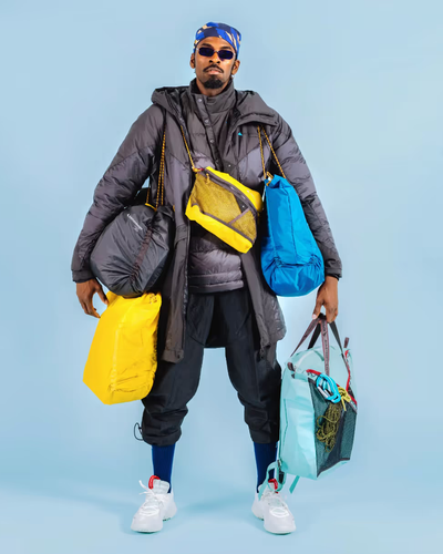 A stylish man wearing many layers of Klattermusen clothing including numerous jackets and bags