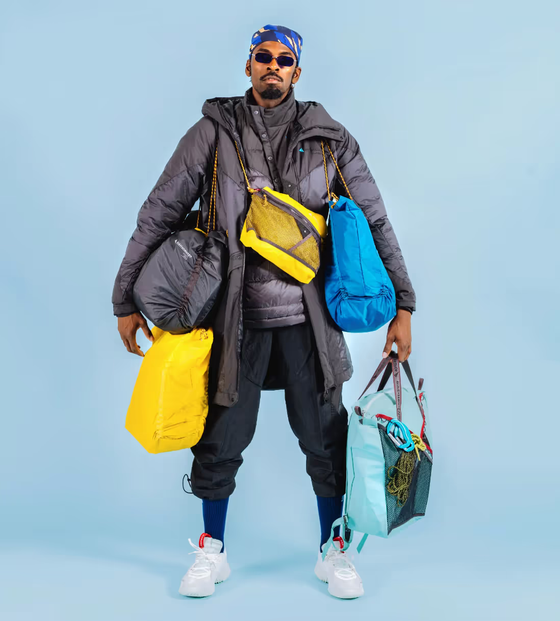 A stylish man wearing many layers of Klattermusen clothing including numerous jackets and bags