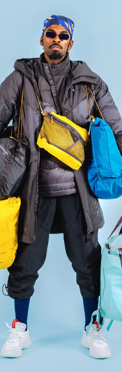 A stylish man wearing many layers of Klattermusen clothing including numerous jackets and bags