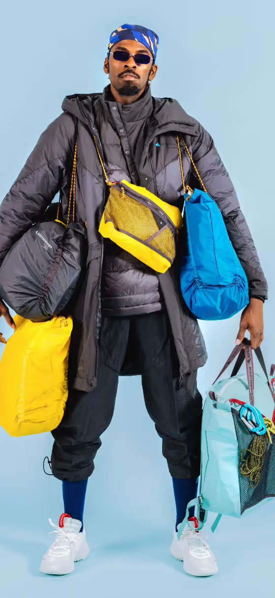A stylish man wearing many layers of Klattermusen clothing including numerous jackets and bags