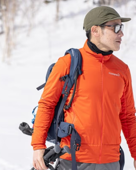 A man looking off in the distance on a snowy mountain wearing an orange Norrona jacket