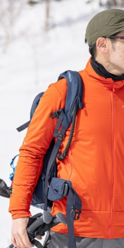 A man looking off in the distance on a snowy mountain wearing an orange Norrona jacket