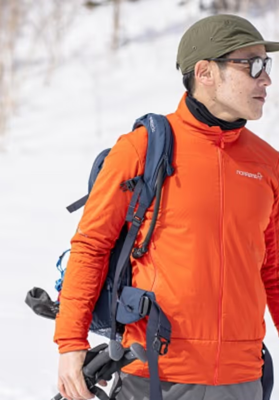 A man looking off in the distance on a snowy mountain wearing an orange Norrona jacket