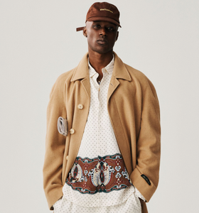 A man wearing a brown Aime Leon Dore trench coat and white button up with a dark brown hat