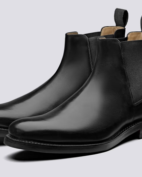 A black pair of Grenson boots that are similar to Blundstones on a white background