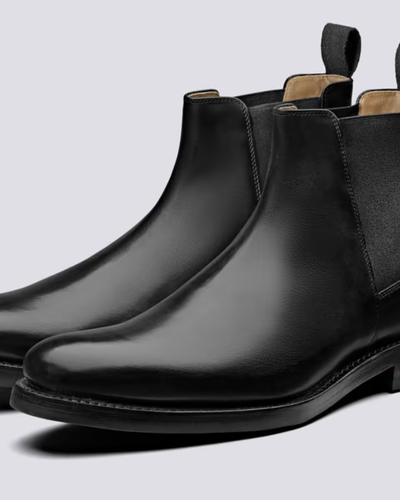 A black pair of Grenson boots that are similar to Blundstones on a white background