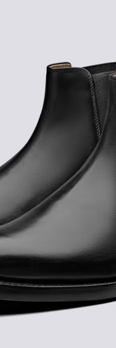 A black pair of Grenson boots that are similar to Blundstones on a white background