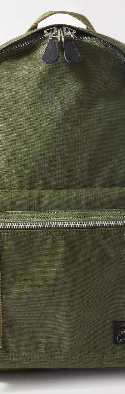 A dark green Porter Yoshida backpack with a silver zipper on a white background