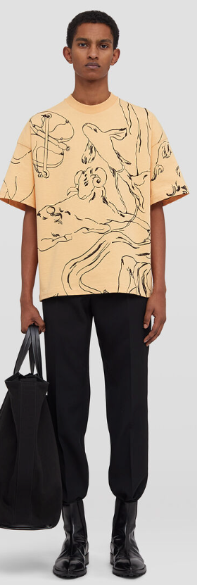 A man wearing a peach colored Jil Sander illustrated short-sleeved t-shirt with black pants and black boots
