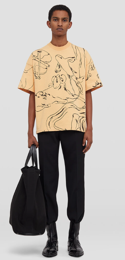 A man wearing a peach colored Jil Sander illustrated short-sleeved t-shirt with black pants and black boots