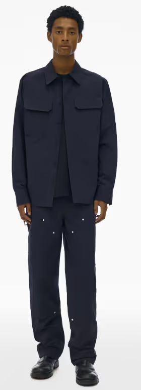 A man wearing a full Navy blue Helmut Lang outfit with a button up top and wide pants and dark navy blue loafers