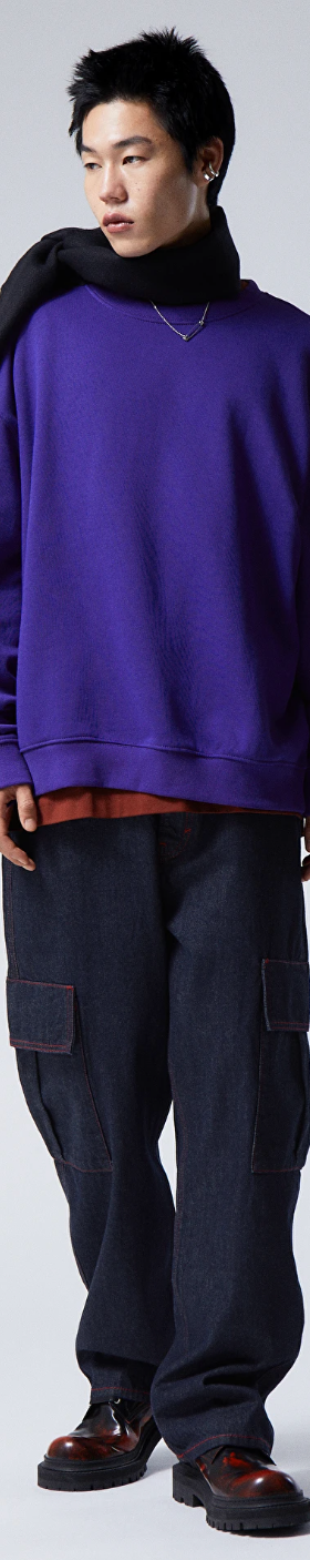 A person wearing a Weekday bright purple sweater, navy blue scarf, denim pants and red and black loafers