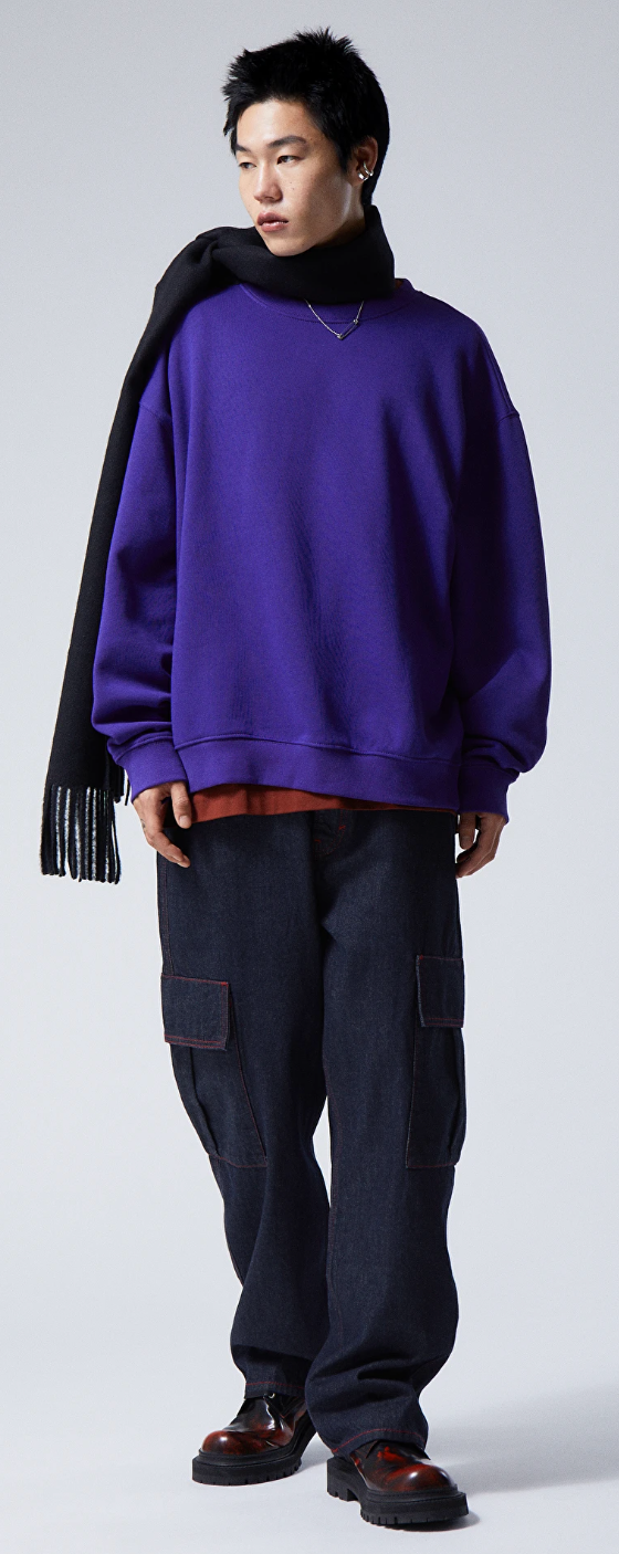 A person wearing a Weekday bright purple sweater, navy blue scarf, denim pants and red and black loafers