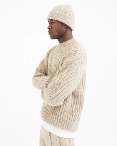 A man wearing a Represent beige knit sweater with a matching beanie and pants