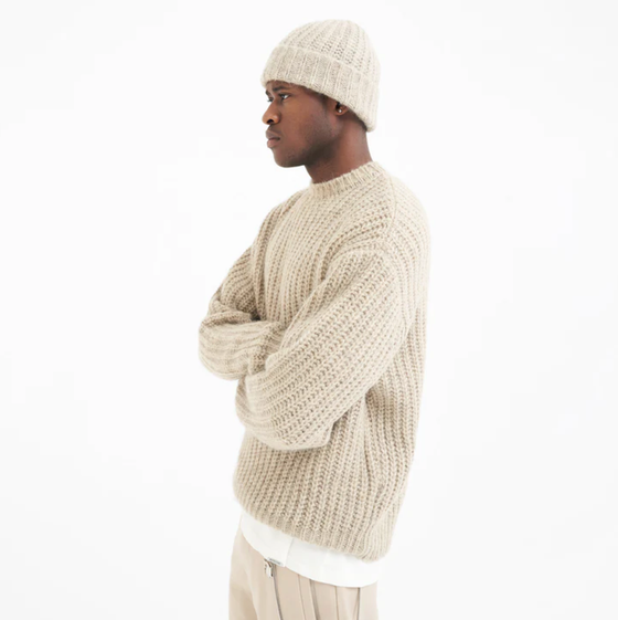 A man wearing a Represent beige knit sweater with a matching beanie and pants