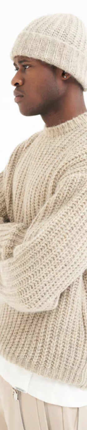 A man wearing a Represent beige knit sweater with a matching beanie and pants