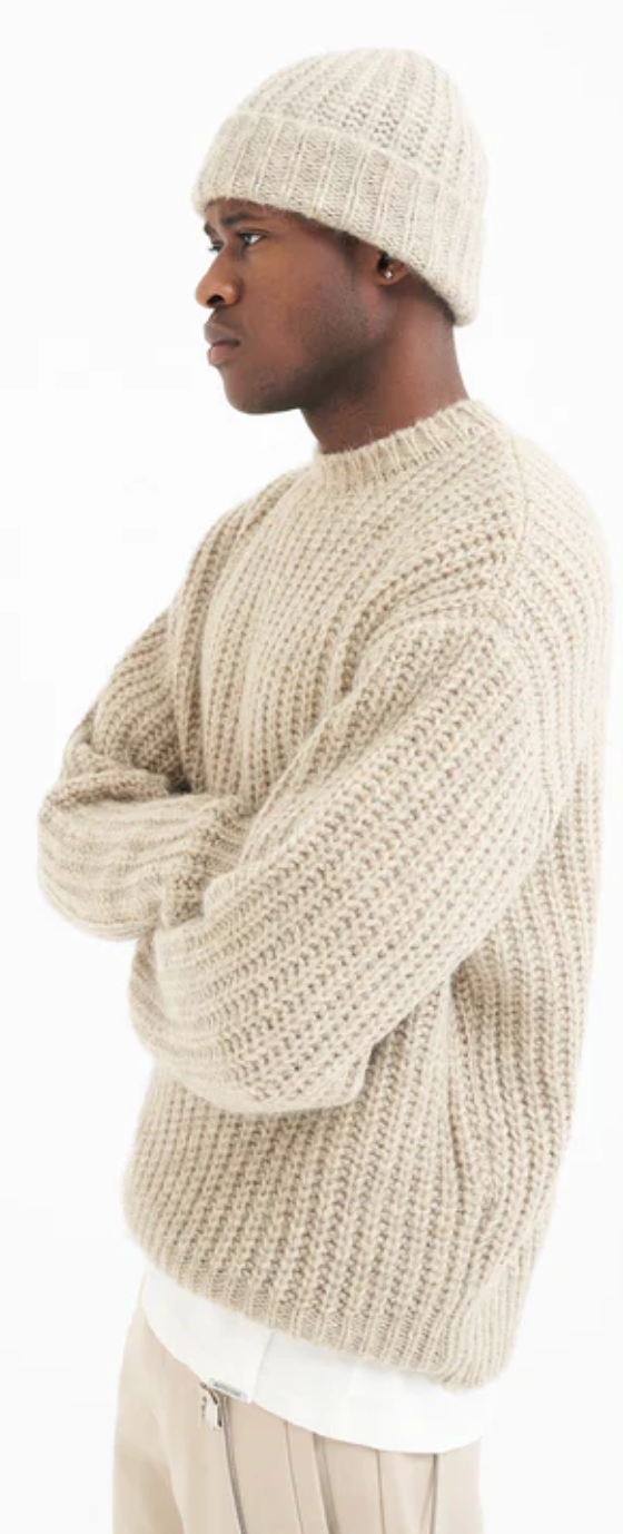 A man wearing a Represent beige knit sweater with a matching beanie and pants