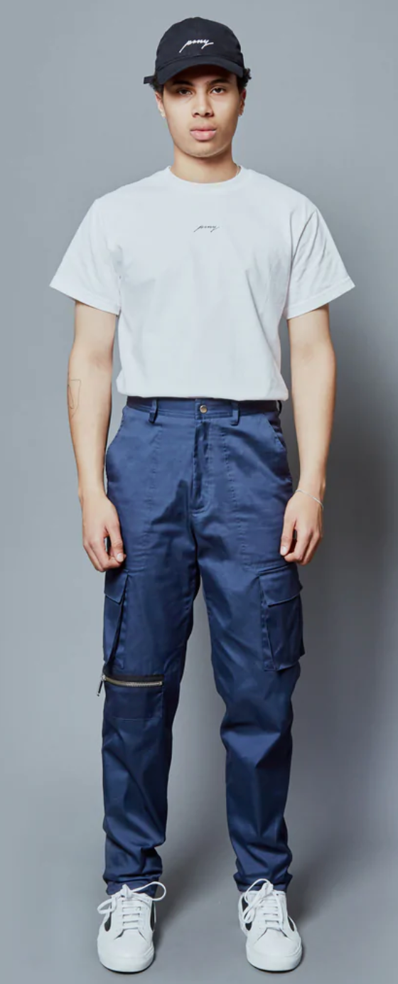 A man wearing a Public School NYC white logo t-shirt and navy blue hat and pants along with white sneakers