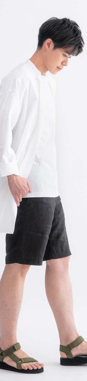 A man wearing a long white Muji button up along with black shorts and olive sandals