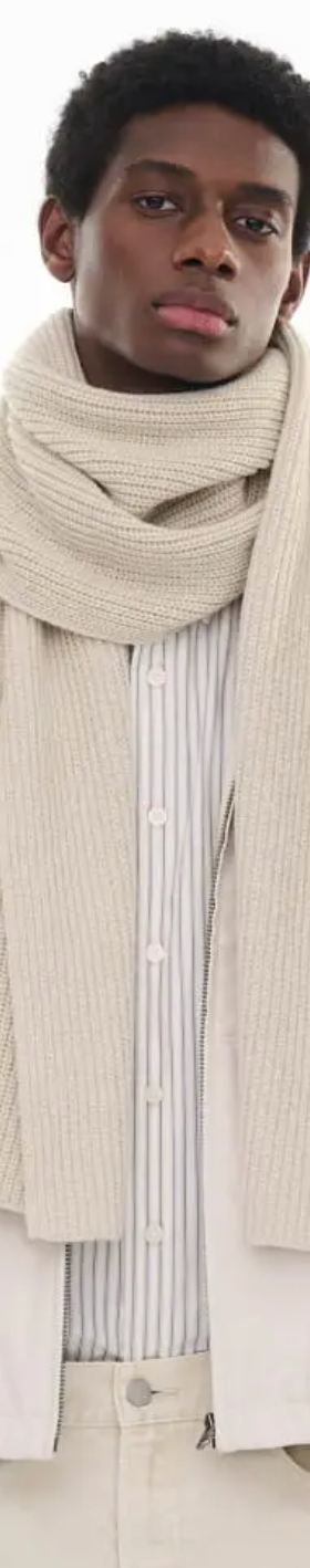 A man wearing an oversize Uniqlo beige scarf with a striped button up and a beige coat
