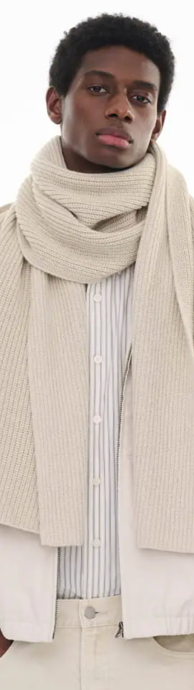 A man wearing an oversize Uniqlo beige scarf with a striped button up and a beige coat