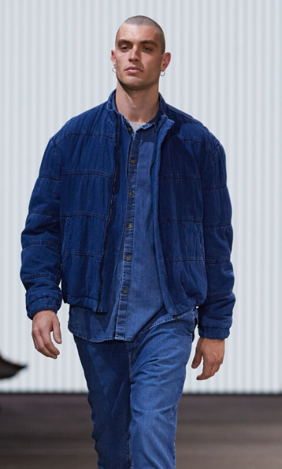 A man walking in a Bassike denim jacket with matching button up and pants