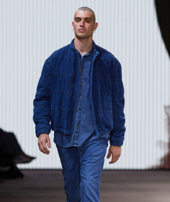 A man walking in a Bassike denim jacket with matching button up and pants