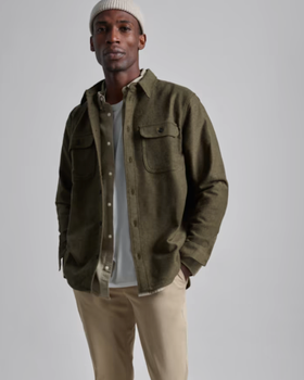 A man wearing a Olive Everlane overshirt, a white beanie and khaki pants