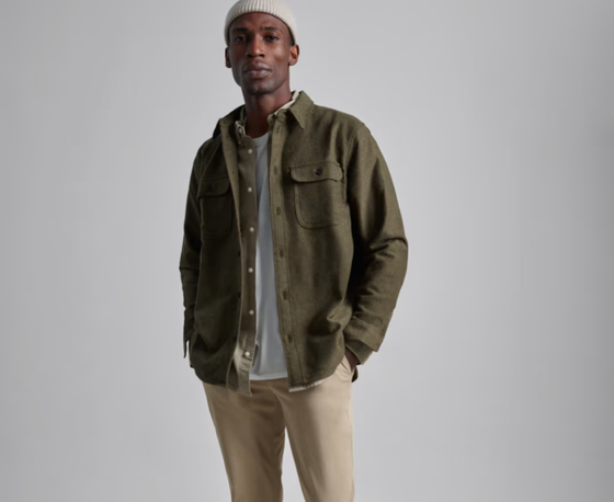 A man wearing a Olive Everlane overshirt, a white beanie and khaki pants