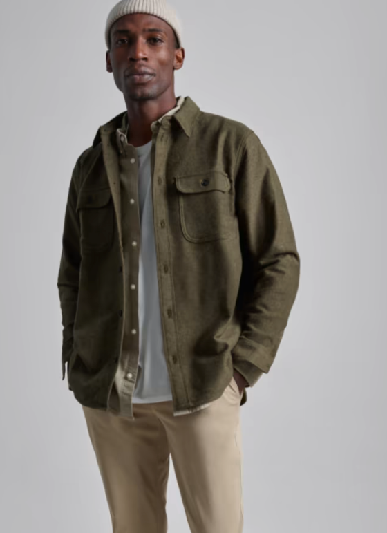 A man wearing a Olive Everlane overshirt, a white beanie and khaki pants