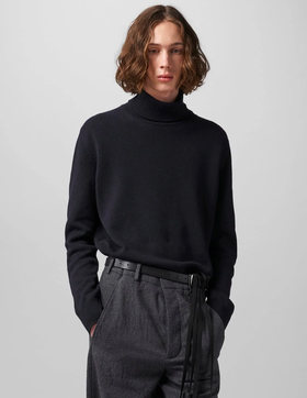 A man wearing a black Ann Demeulemeester turtleneck with a belt and dark grey dress pants