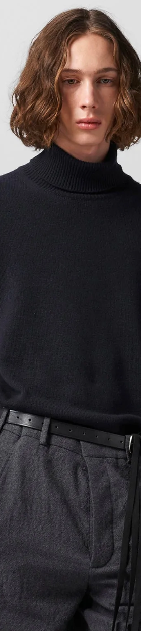 A man wearing a black Ann Demeulemeester turtleneck with a belt and dark grey dress pants